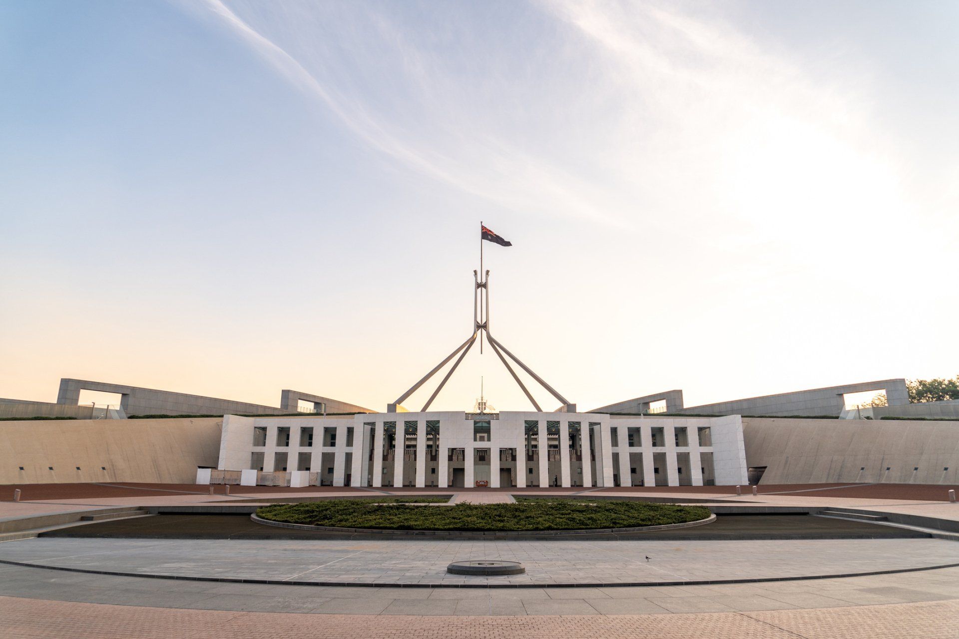 Australian Parliament House, Canberra, with flag, against a blue sky at sunset.